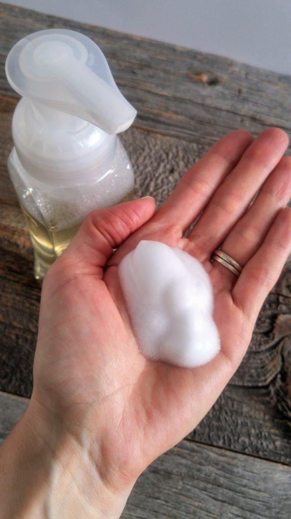 A hand holds a pump of foamy hand soap