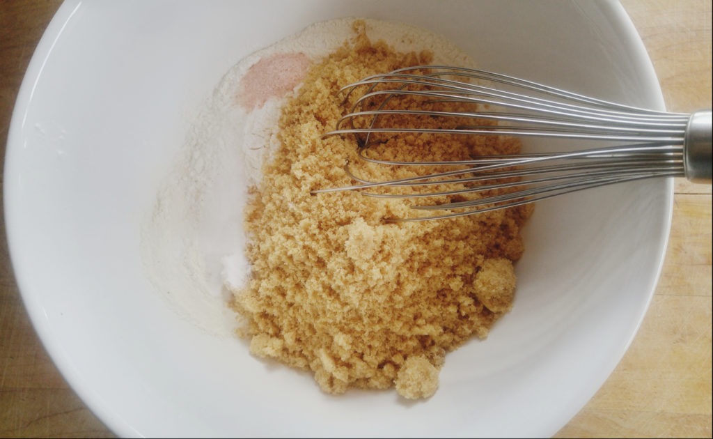 A wisk blends dry ingredients in a white ceramic bowl.