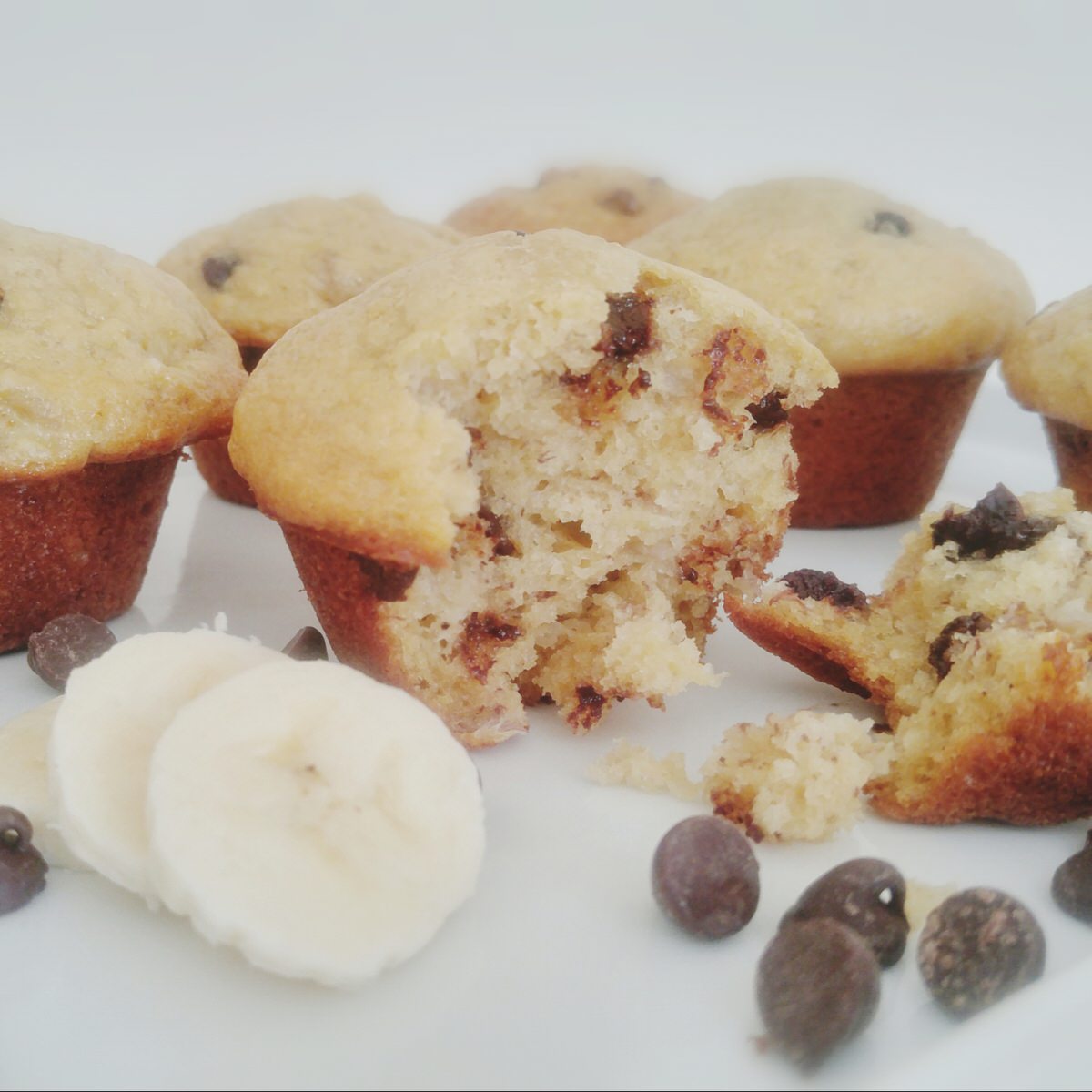 banana chocolate chip muffins on a white plate with one broken in half to show texture