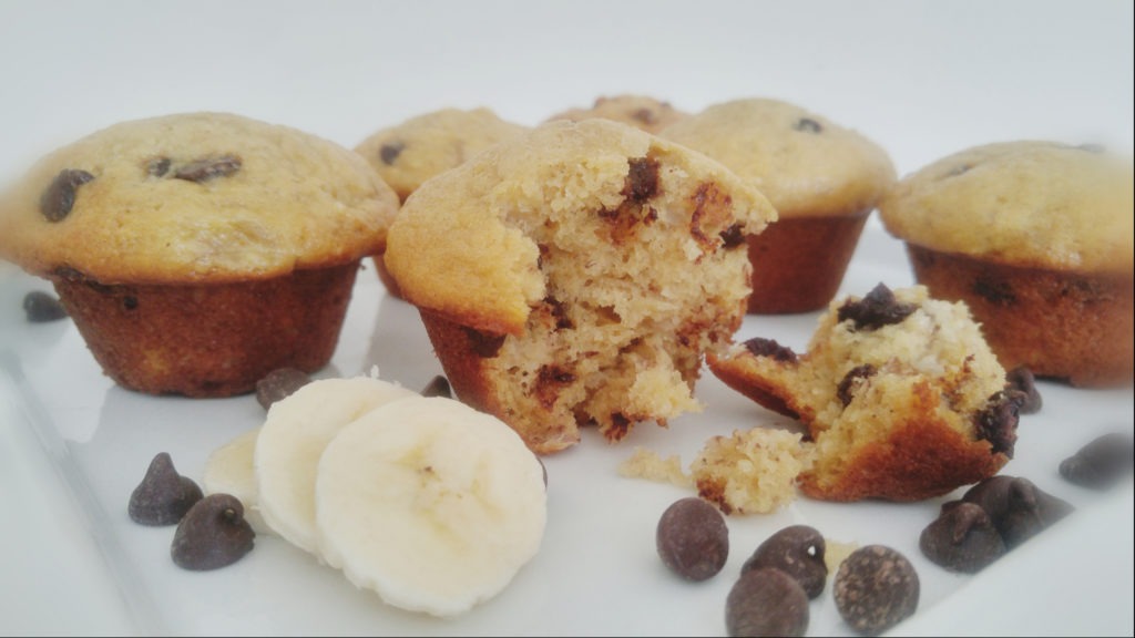 banana muffins with chocolate chips on a white plate. One muffin is split in two.