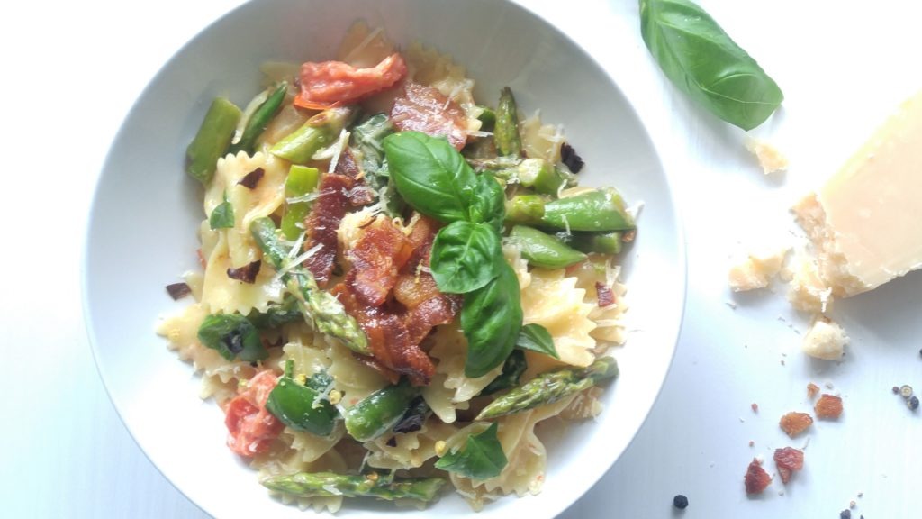 Close up of spring bowtie pasta, bacon and veggies in a white bowl.