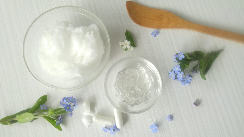 bowls of cream and clear gel sit on a table with open vitamin cases and some small flowers scattered around