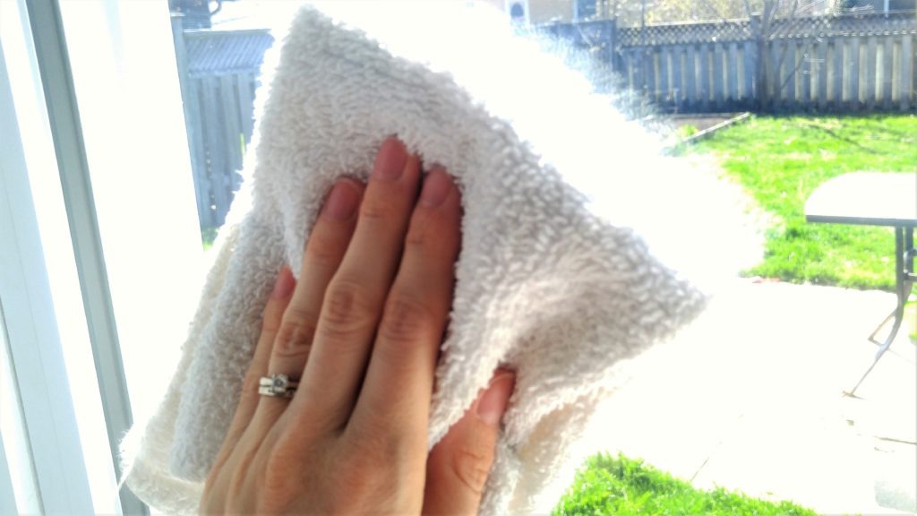 A close up of a hand holding a white cloth, wiping a window to clean it on a sunny day.
