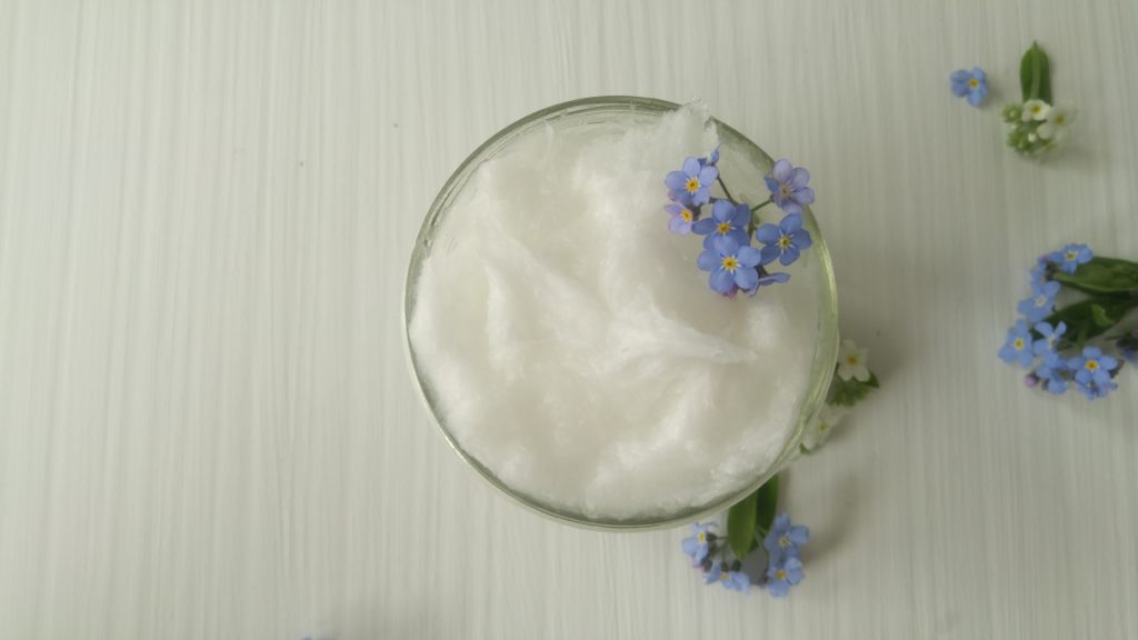 looking down at an overfilled jar of moisturizer with a few forget-me-not flowers on top.