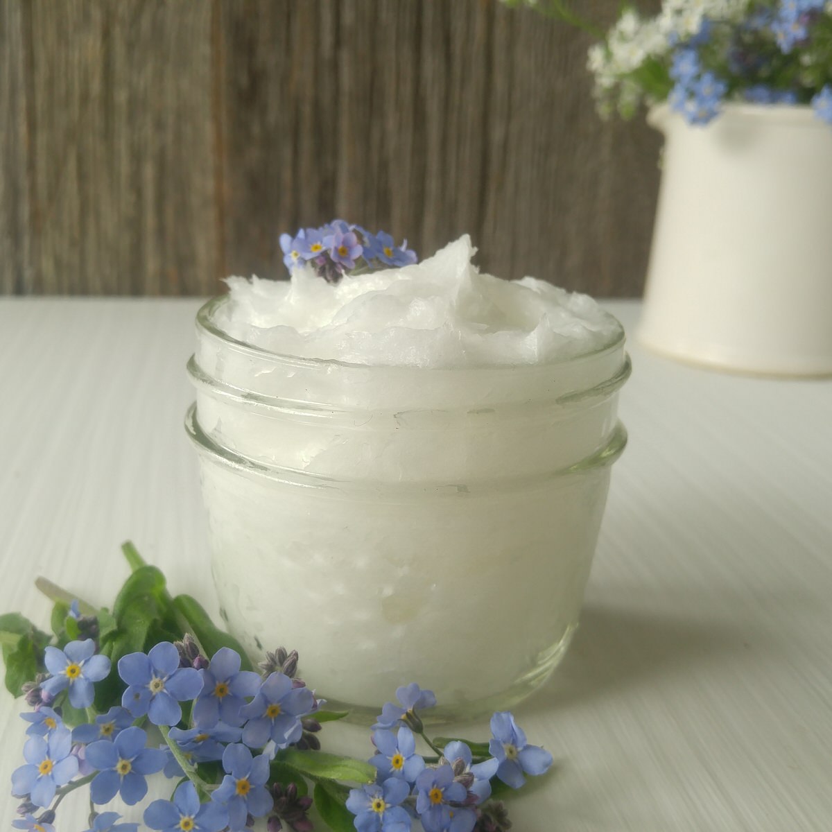 small mason jar filled with wrinkle-reducing whipped nightly moisturizer on a white table with tiny blue flowers around it