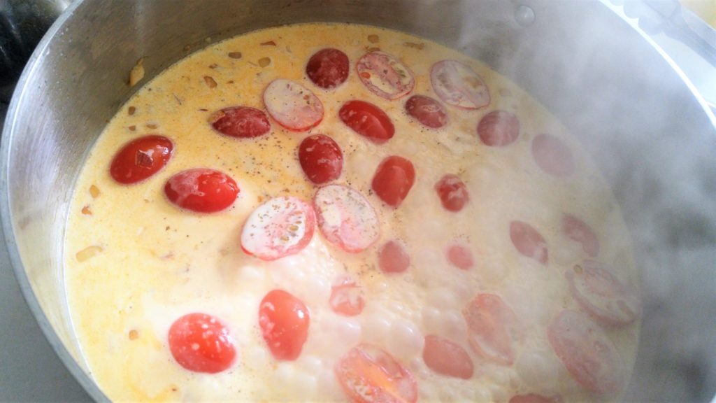 A close up of a stainless steel pot with bubbling cream and cherry tomatoes in it.