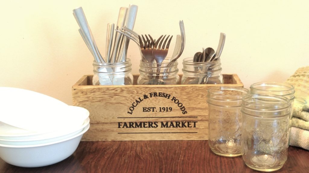 A table with mason jars, cereal bowls, and a rustic wooden box filled with cutlery.