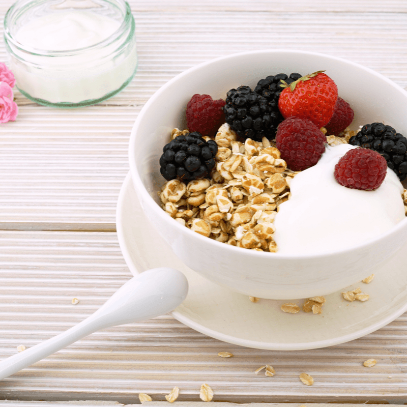 A white bowl on a table filled with museli, berries, and yogurt.