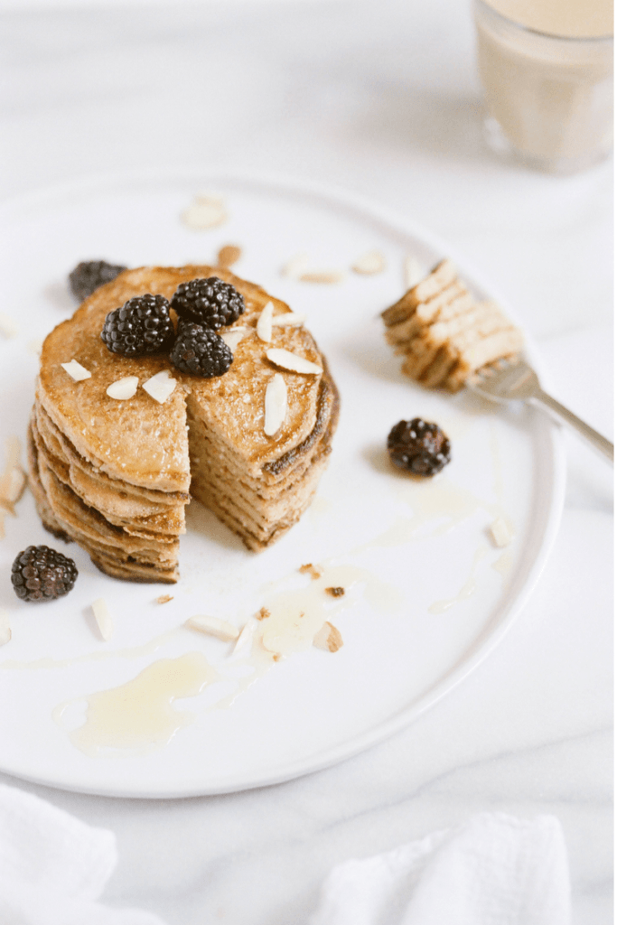 a plate of a stack of pancakes with fresh blackberries, almonds, and honey on top.