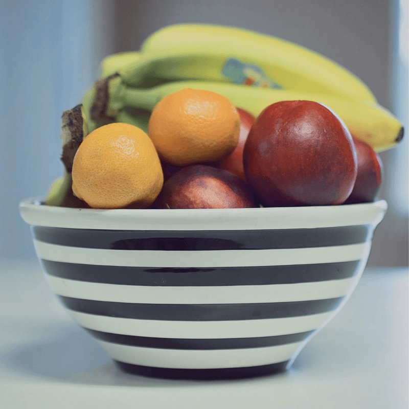 Close up of a ceramic bowl full of apples, oranges, and bananas.