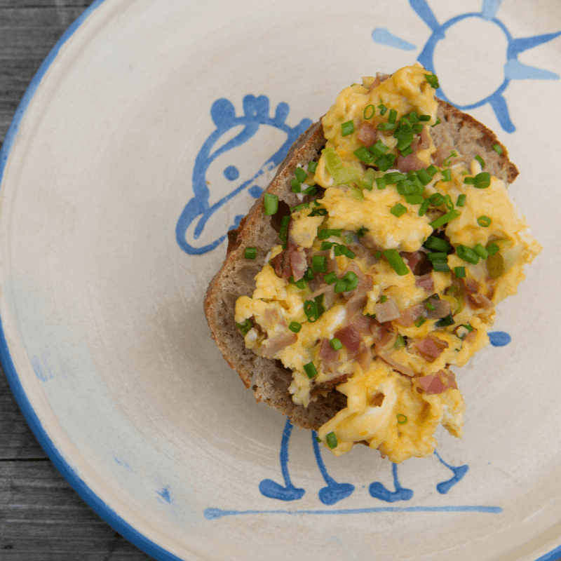 scrambled eggs with bacon and chives sitting on a piece of toast on a plate