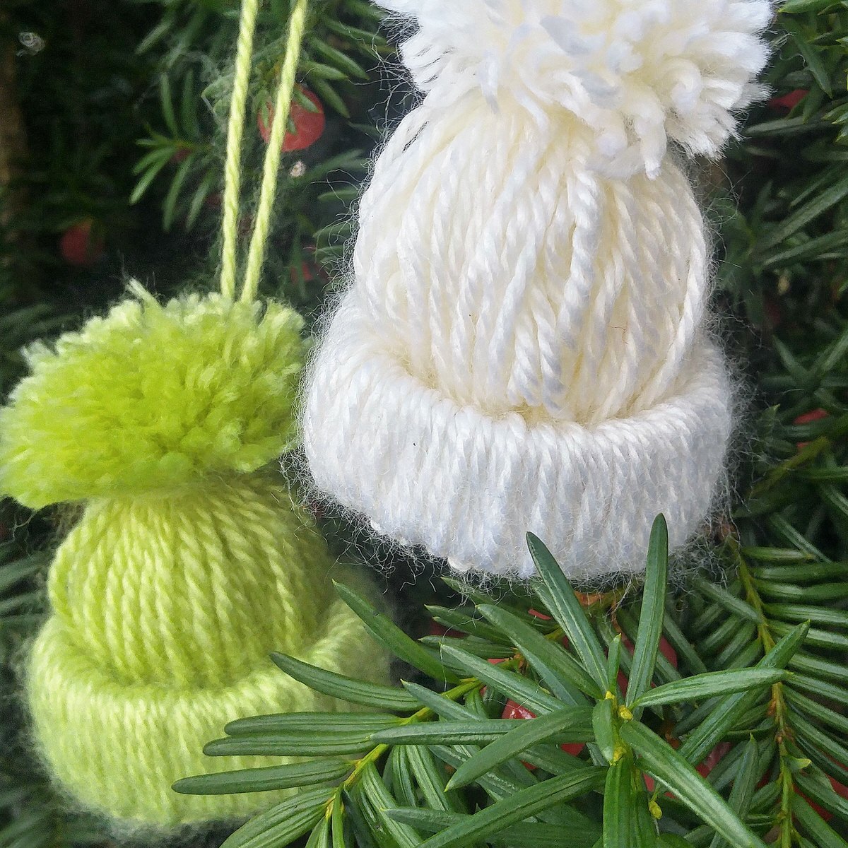 close up of a green and a white winter had ornament hanging on an evergreen tree