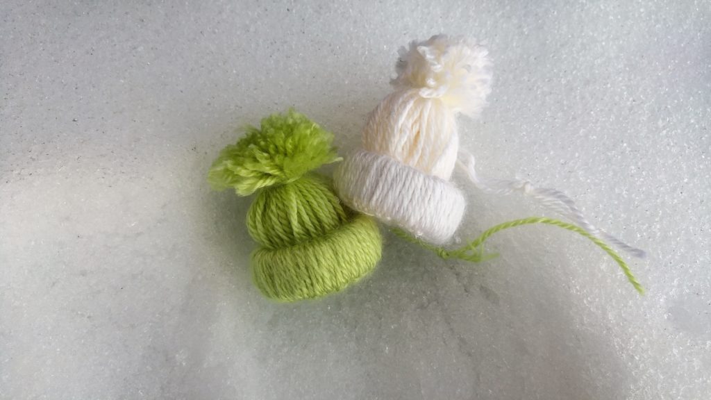 A green and a white completed hat ornament lie in snow.