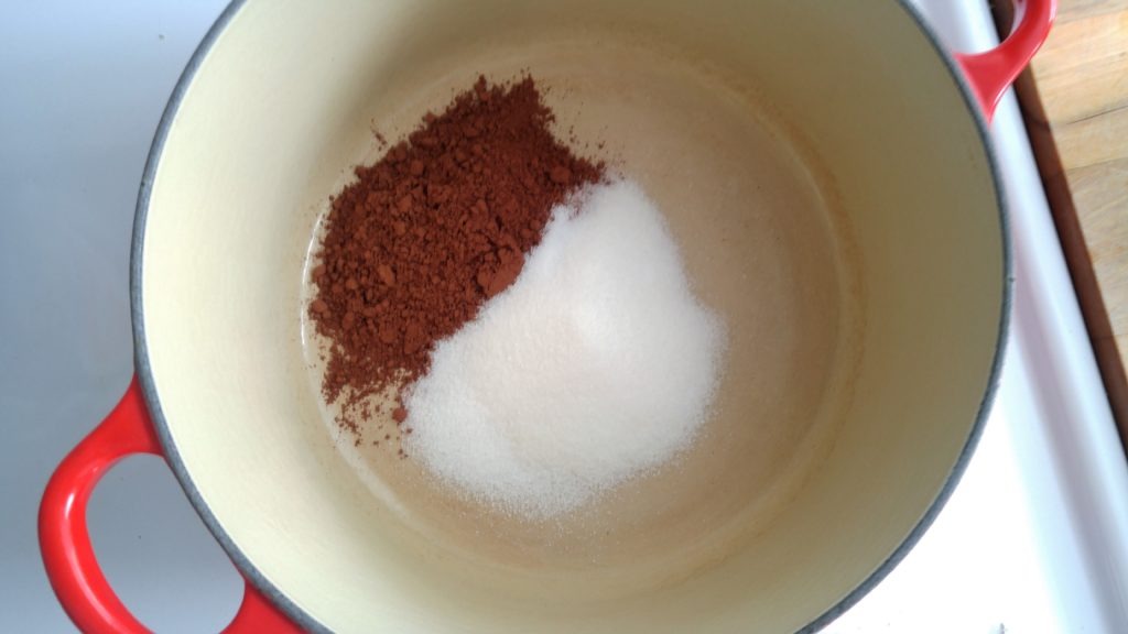 A red ceramic pot sits on a burner with cocoa and sugar inside.