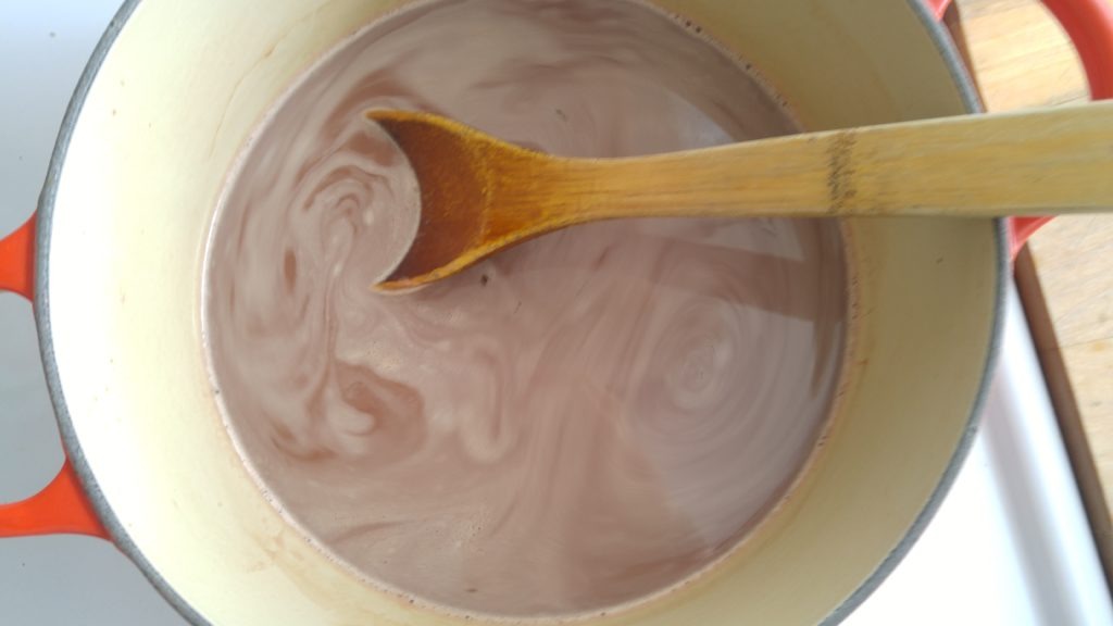 creamy hot chocolate cooking in a pot with a wooden spoon in it to stir.
