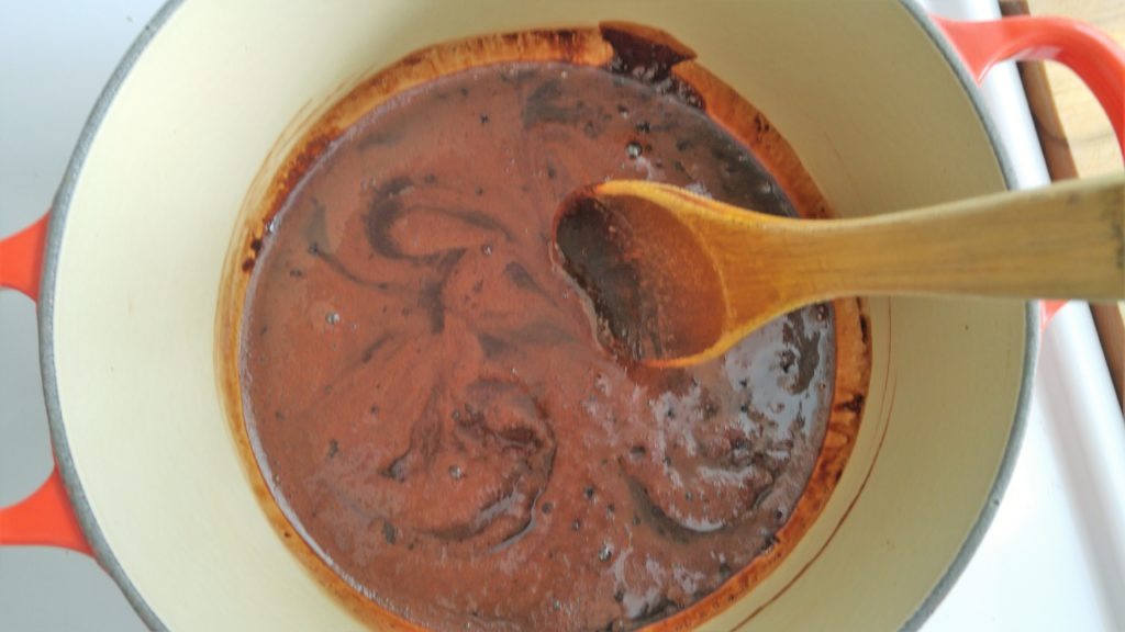 Looking into a pot with brown liquid being stirred with a wooden spoon.