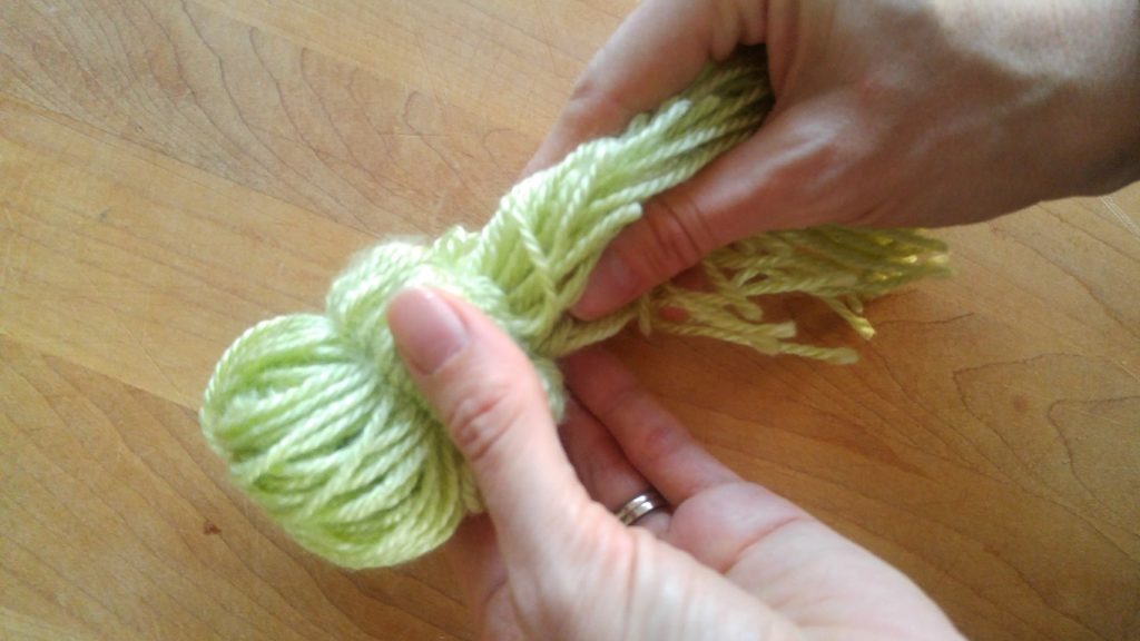 Hands demonstrating how to pull all the strands of yarn into the ornament.