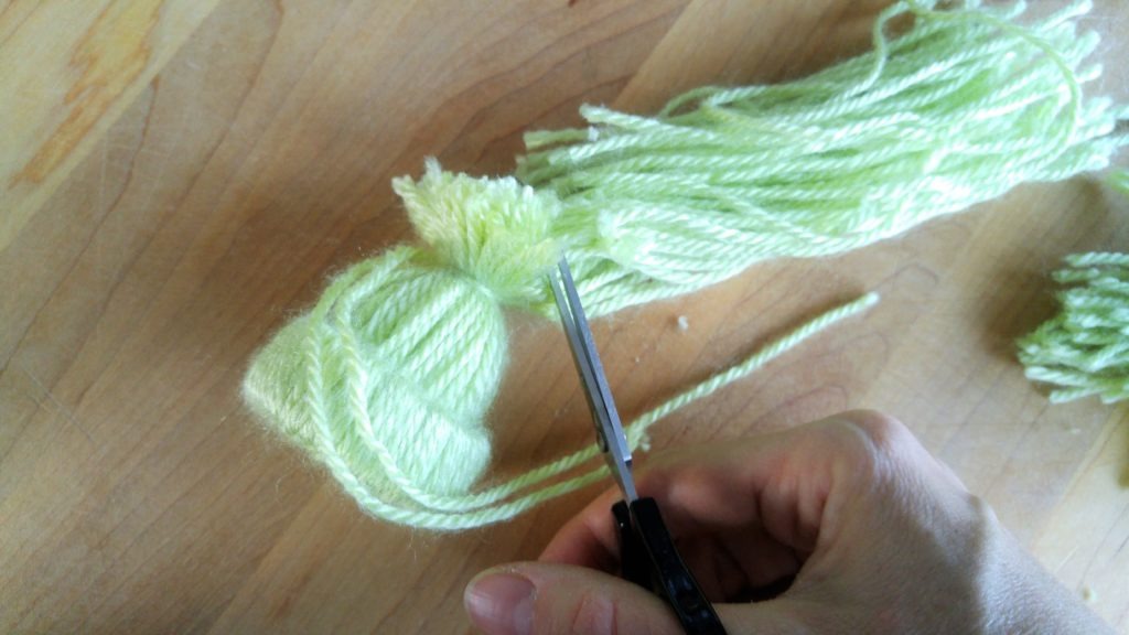 Scissors trim the excess yarn away from the end of the hat ornament.