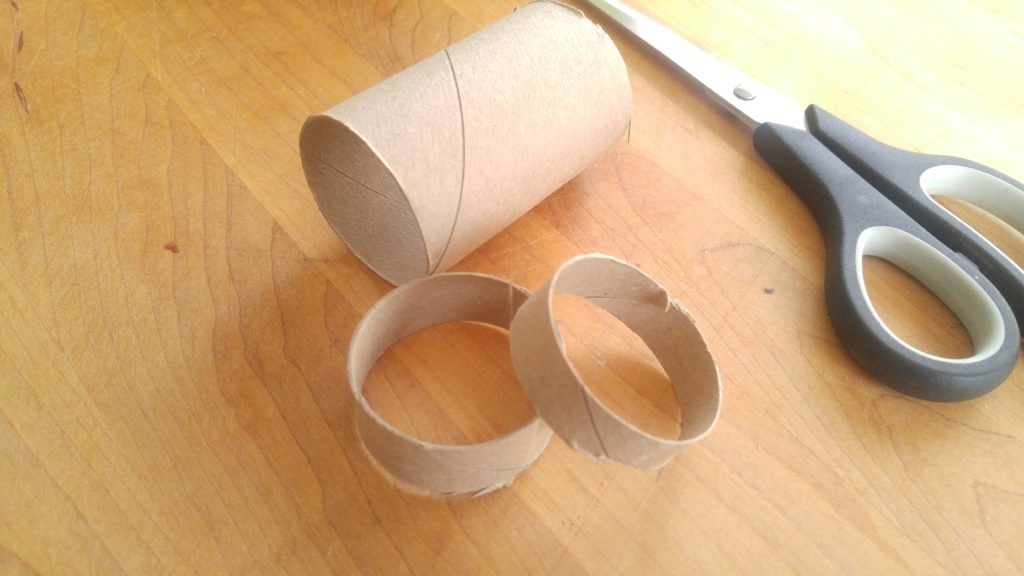 Round slices of a toilet paper roll on a cutting board beside a pair of scissors.