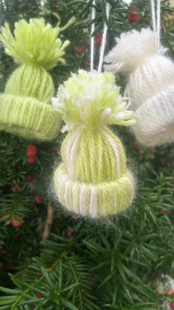 Three winter hat ornamnets close up on a evergreen tree.