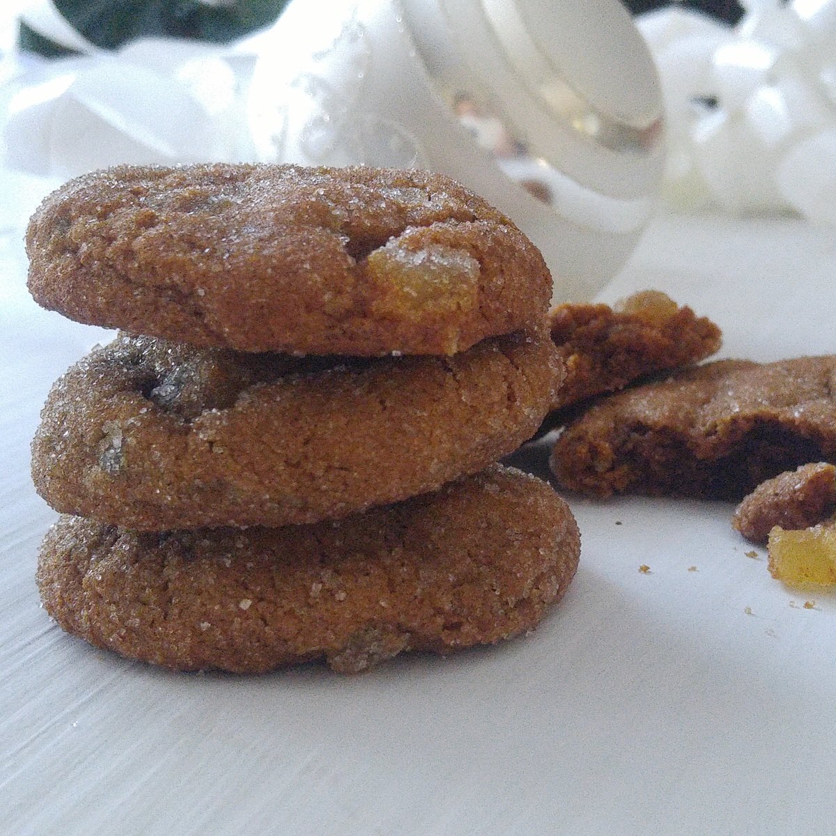 a pile of three chewy gingersnap cookies sit on a white table in front of a christmas tree