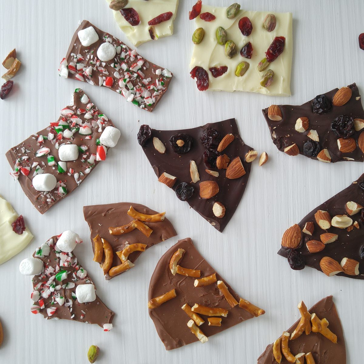broken pieces of chocolate bark scattered around a white countertop include milk white and dark chocolate