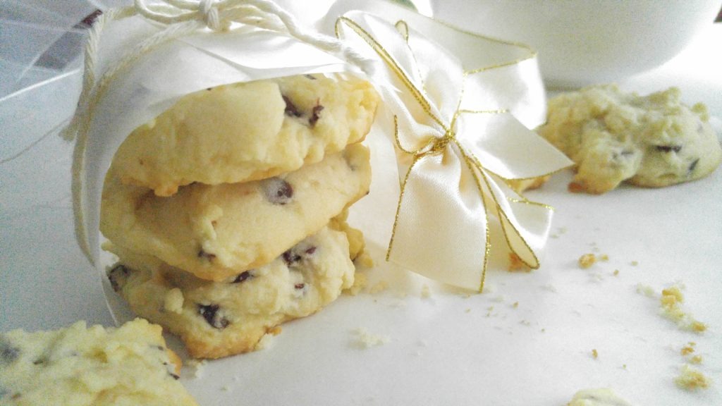 A stack of 3 shortbread cookies sit on a white table wrapped in parchment and a white ribbon.