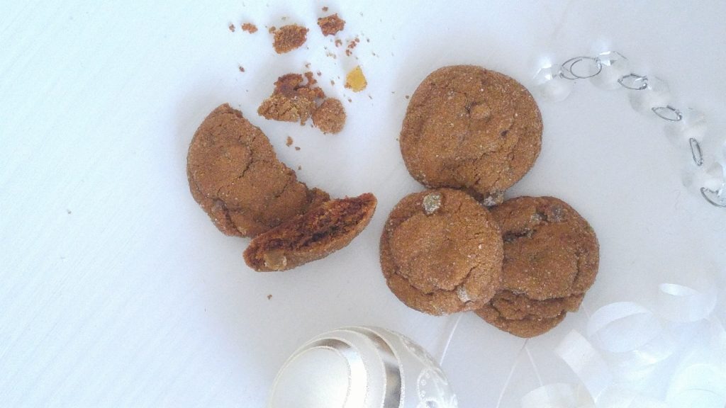 Looking down at 3 gingersnap cookies on a white table surrounded by white christmas ribbon