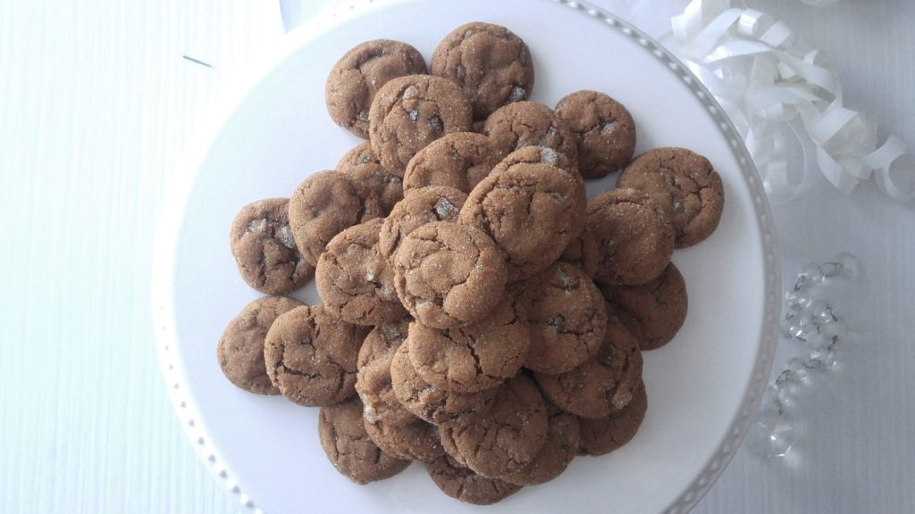 a pile of gingersnap cookies sits on a white cake stand.