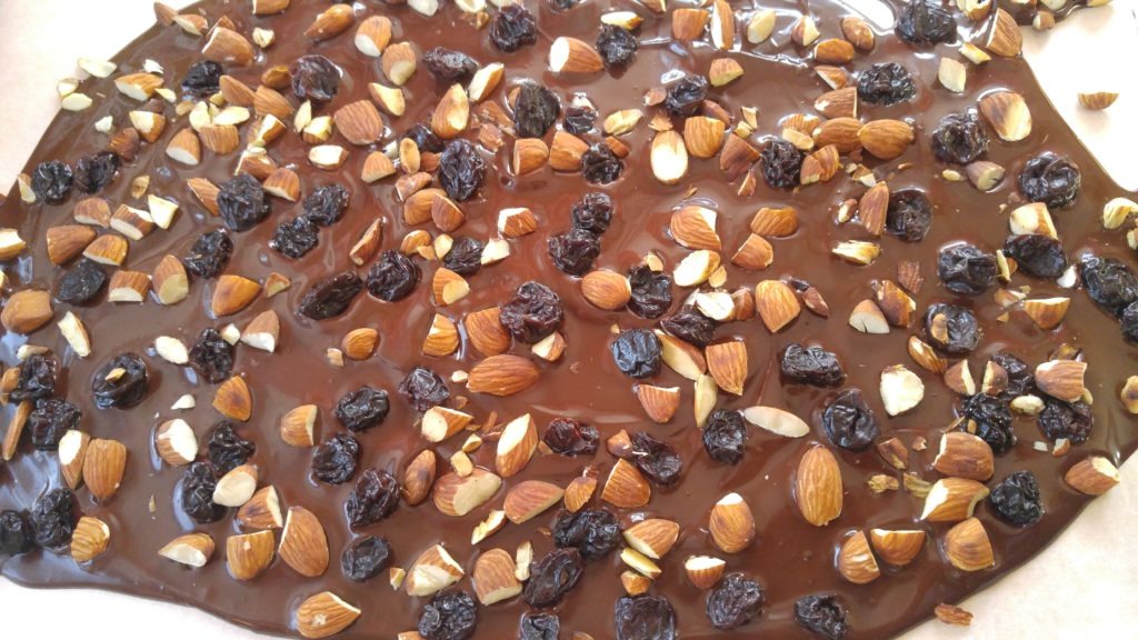 A close up shot of milk chocolate bark topped with rasins and chopped almonds.