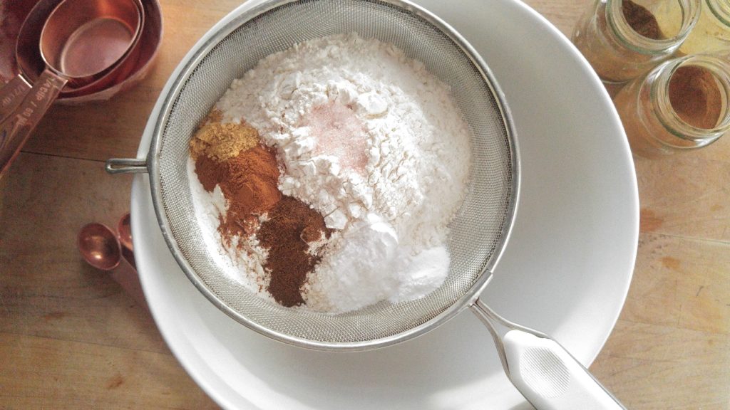 Dry ingredients for gingersnap cookies in a sifter set over a white bowl.