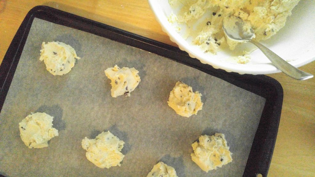 Raw spoonfuls of cookie dough are on a parchment-lined baking sheet.