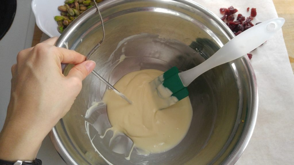 a hand holds a thermometer into a bowl of melted white chocolate.