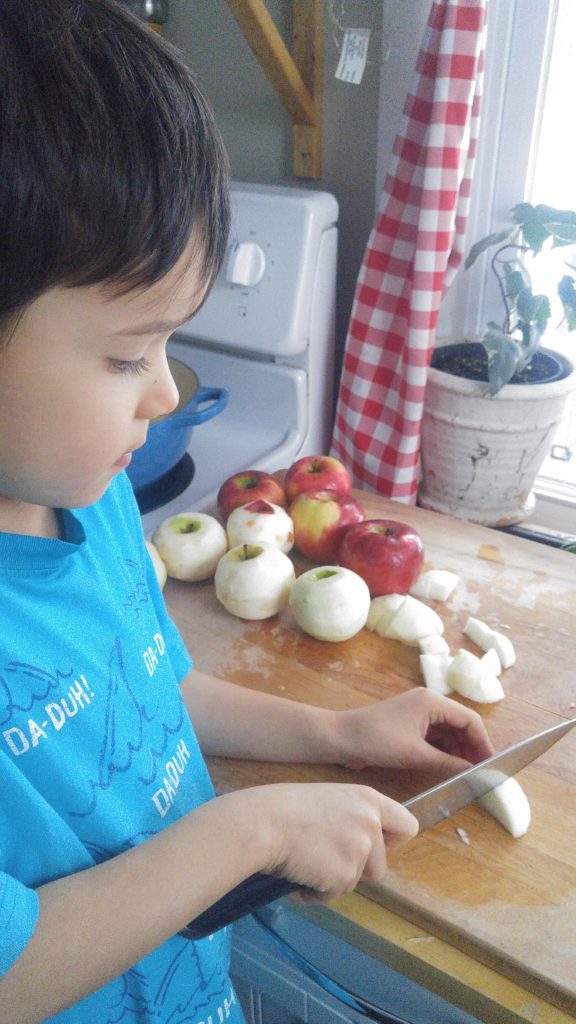 a young boy chops apples into slices on a cutting board.