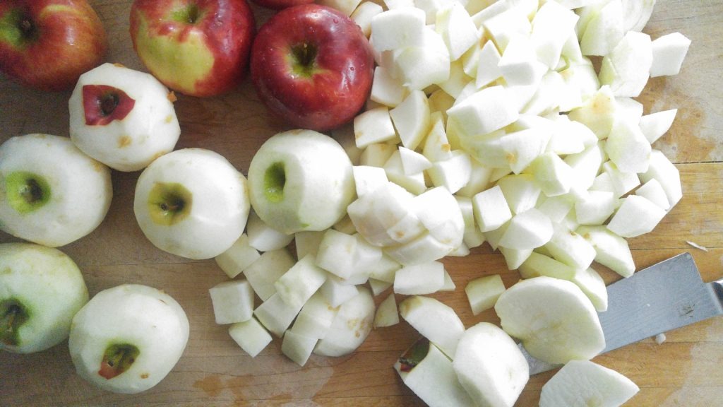 a close up shot of whole unpeeled apples, peeled apples, and some apples cut into one inch pieces.