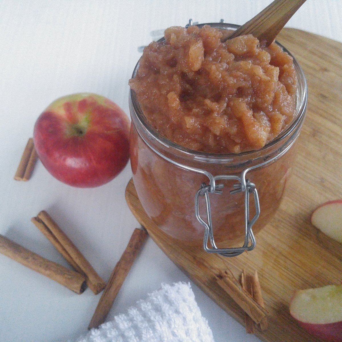 clear glass jar full of easy homemade cinnamon applesauce sitting on a cutting board surrounded by apple slices and cinnamon sticks