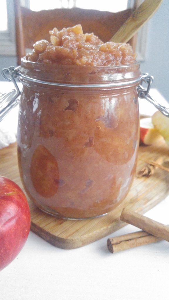 close up of a glass jar full of cinnamon applesauce sitting on a cutting board.
