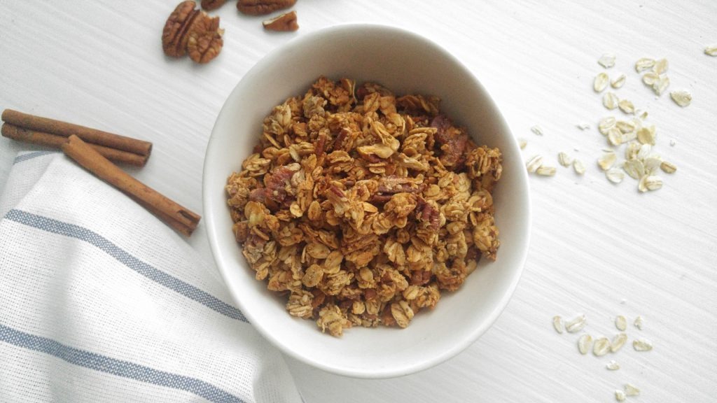 close up of a bowl of crispy granola with cinnamon sticks and oats beside it