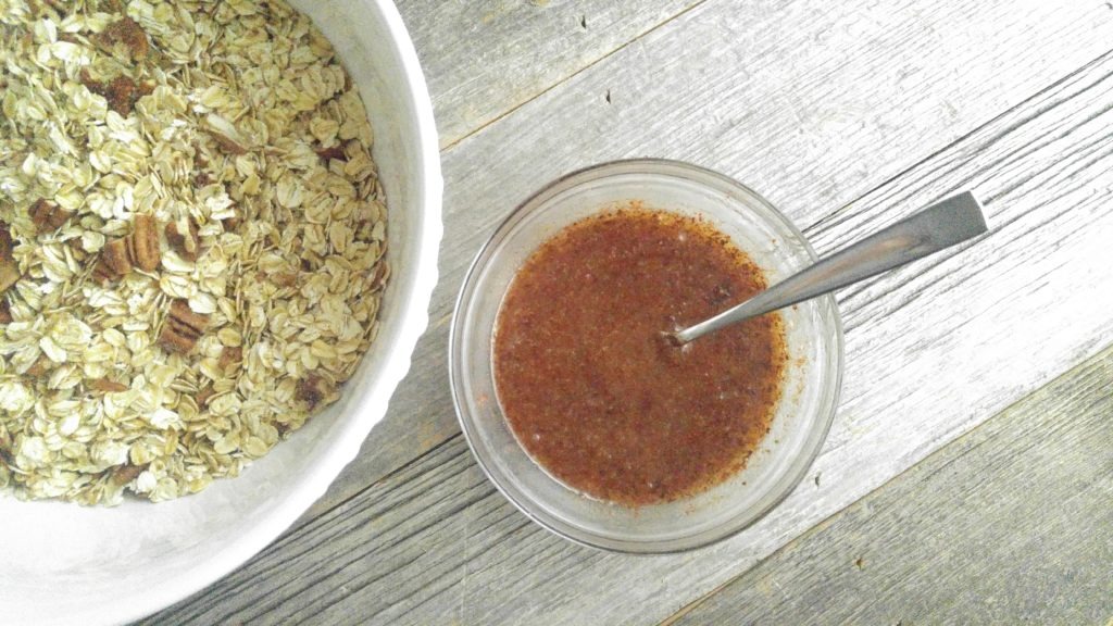 wet ingredients in a small glass bowl placed beside a white bowl full of oats and pecans