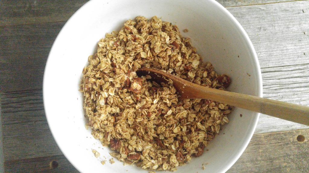 close up picture of uncooked, moist granola with a wooden spoon in the bowl for stirring 