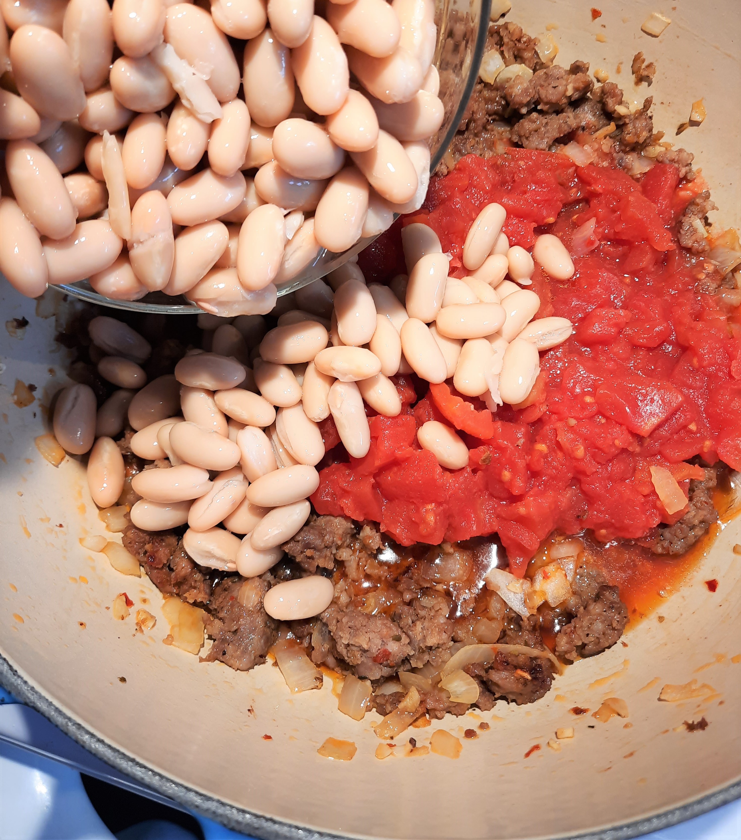 white beans added to a pot with cooked sausage meat and canned tomatoes
