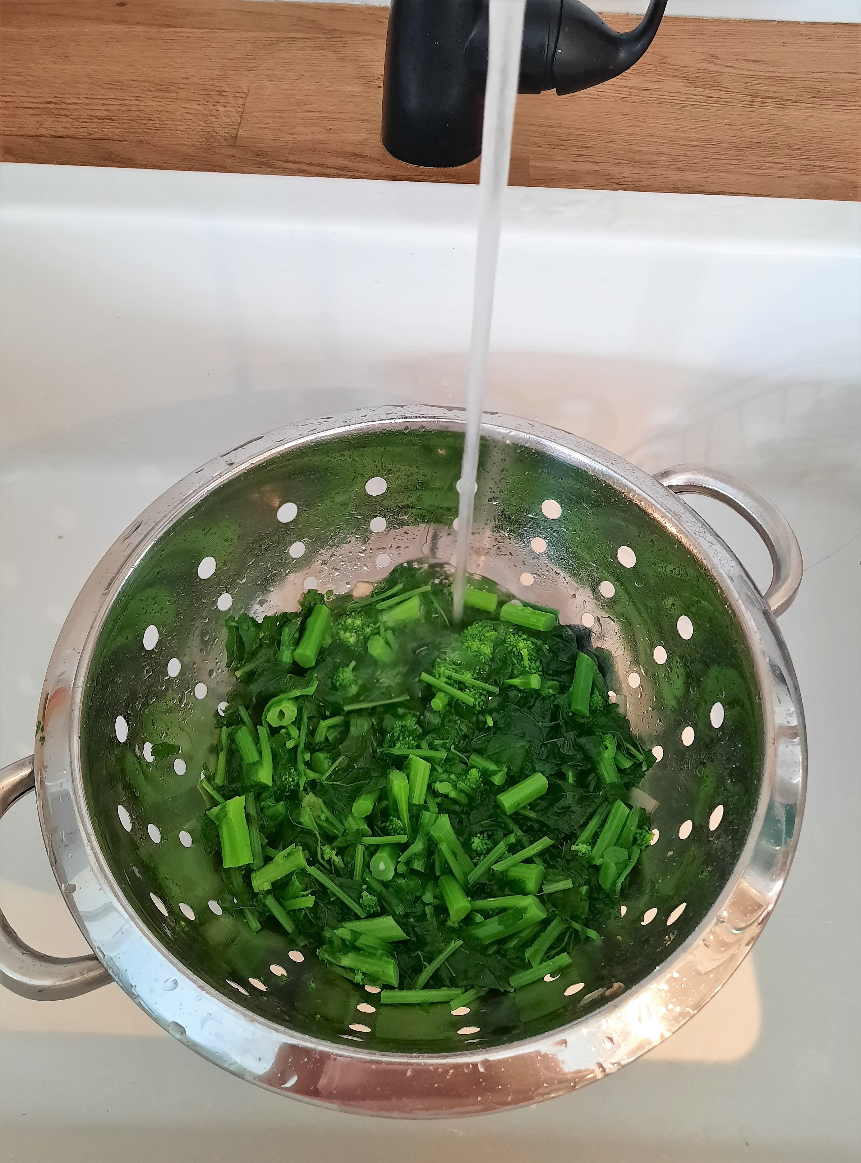rapini in a colander under running tap water