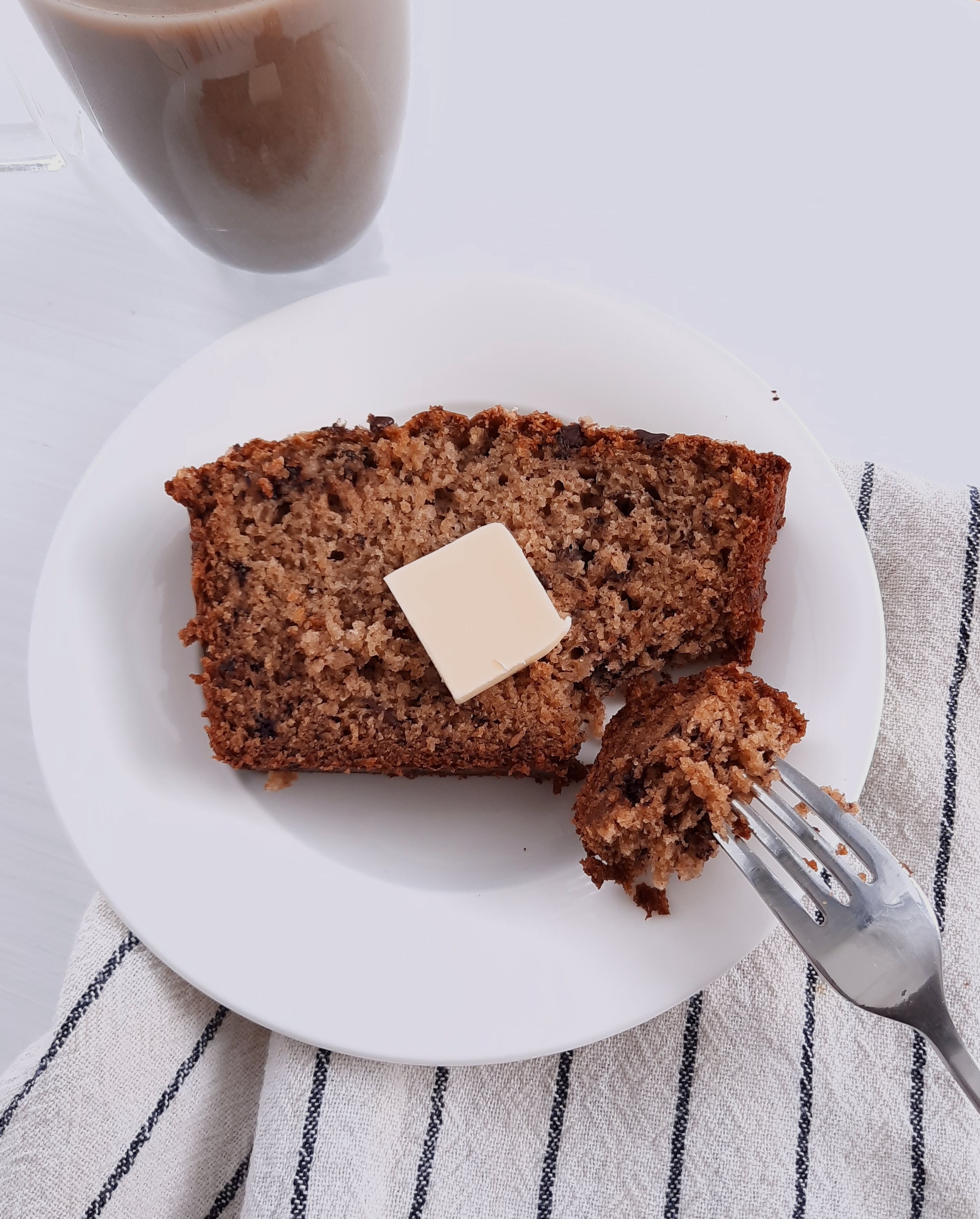 Fork with best banana bread on it beside a piece of banana bread with butter