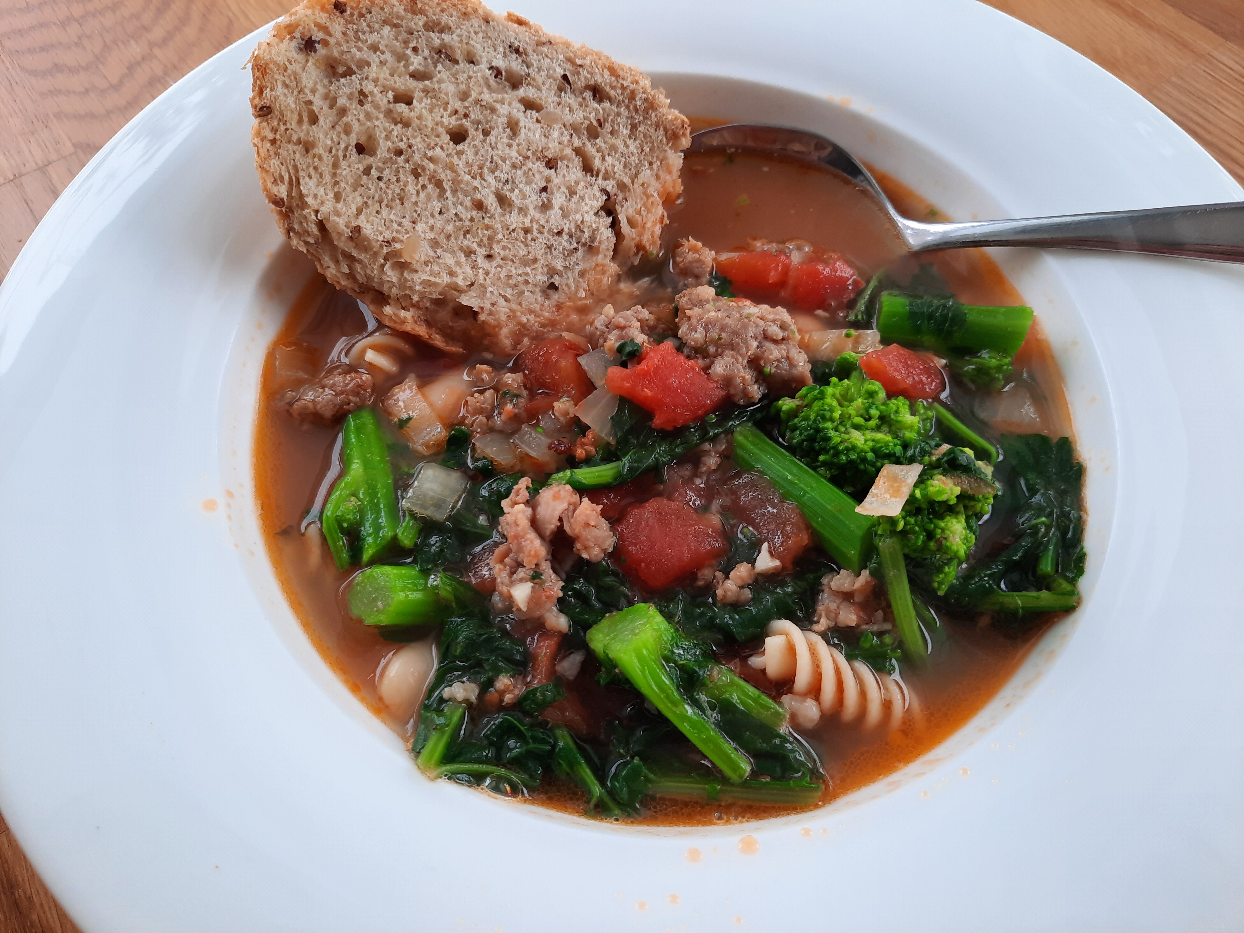 bowl full of hearty sausage, white bean, and rapini soup with a slice of bread