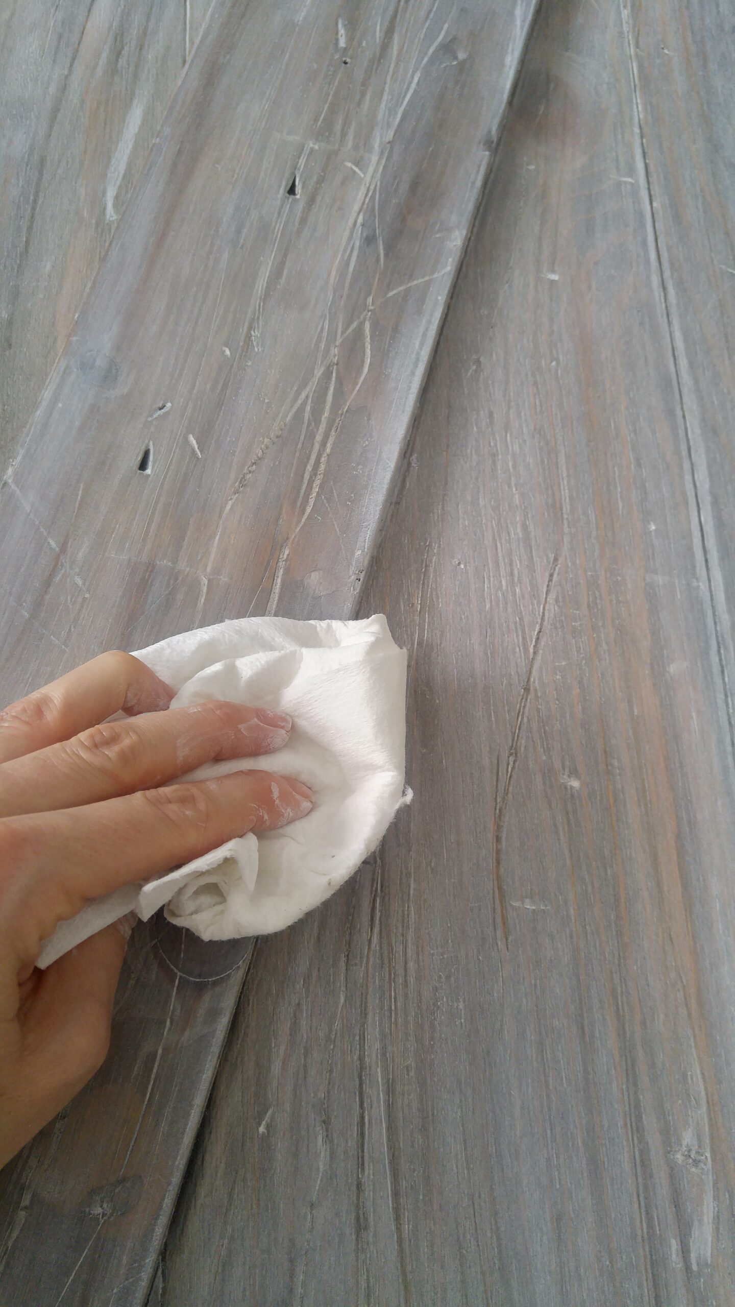 a hand wipes off some white paint off barn door using a clean white cloth