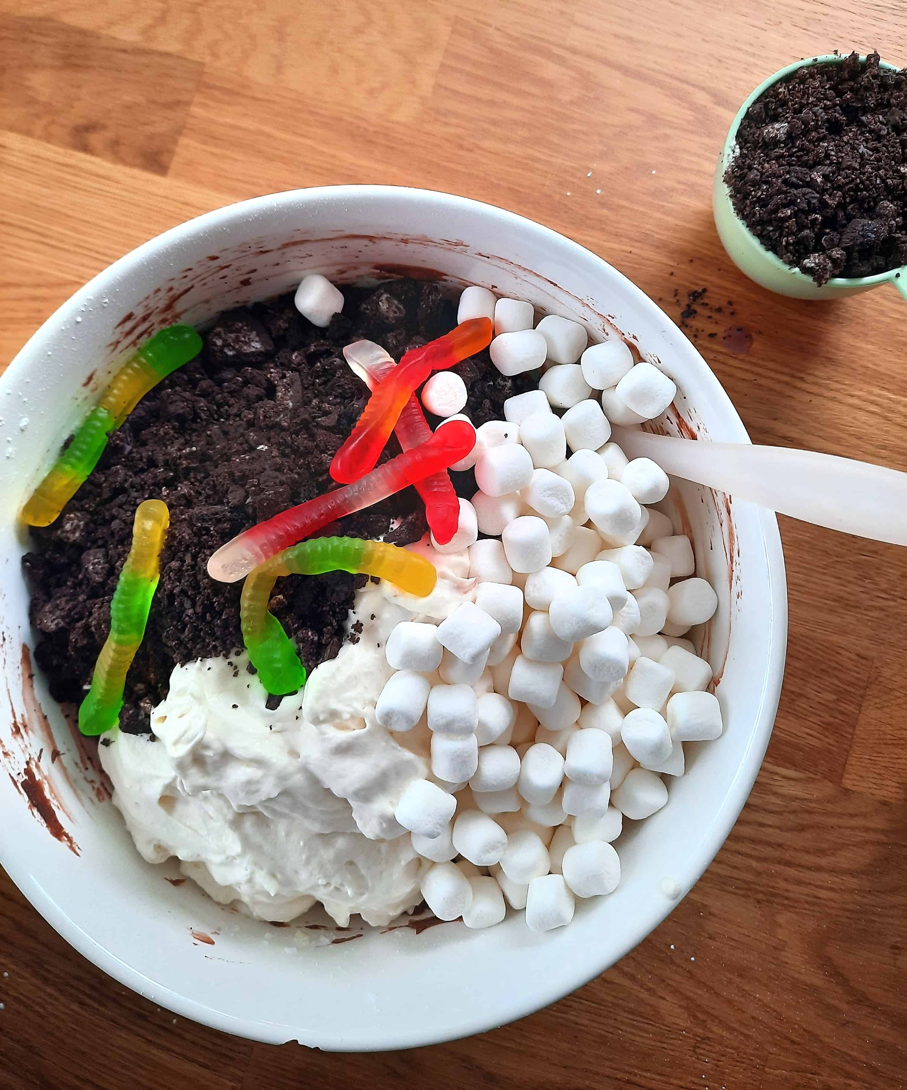 Large white bowl full of marshmallows, whipped cream, and gummy worms