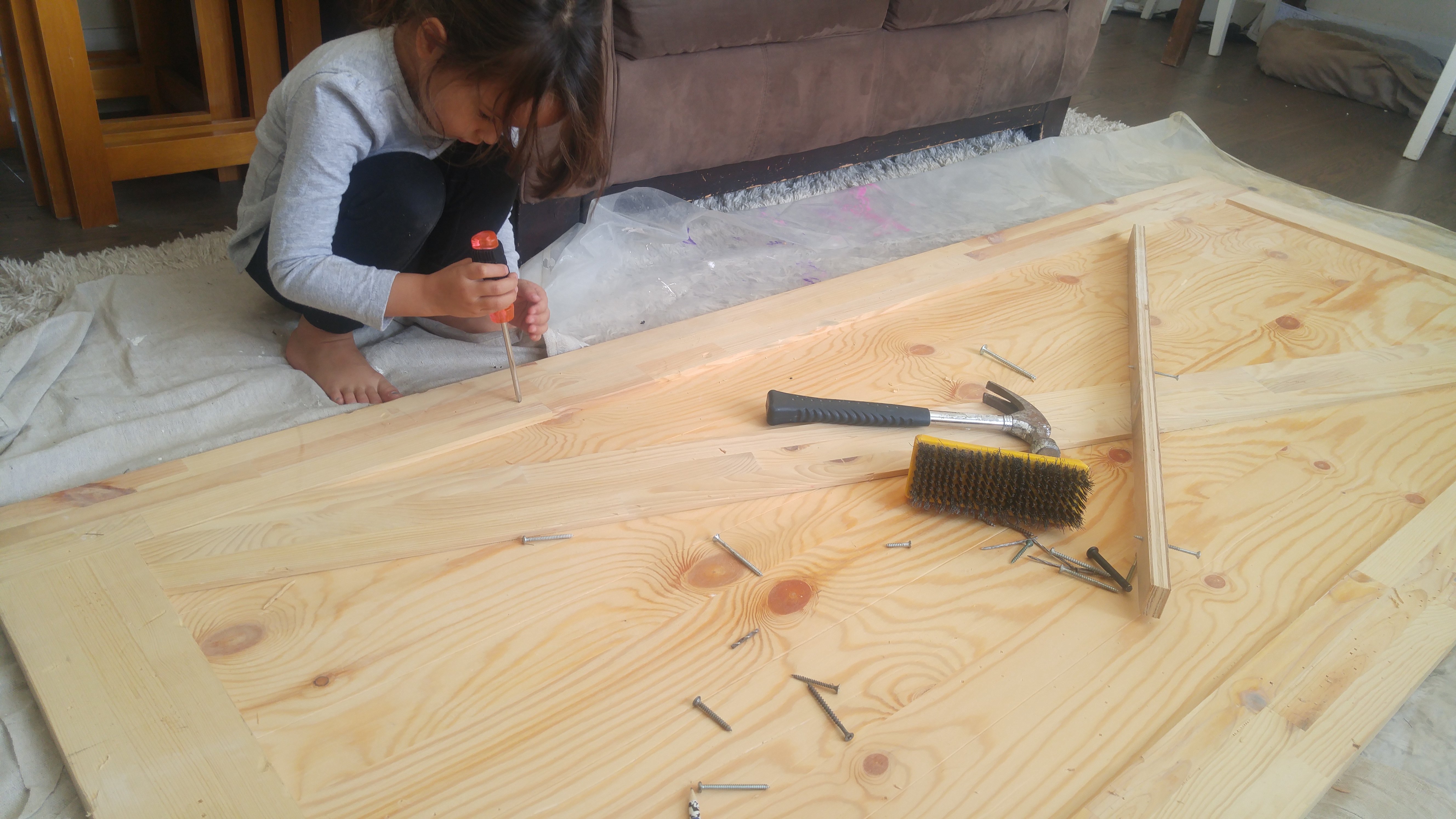 little girl hammers into unfinished barn door to give it a weathered appearance