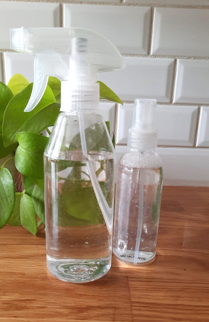 clear spray bottle and small spray bottle sit on a counter full of clear natural cleaners