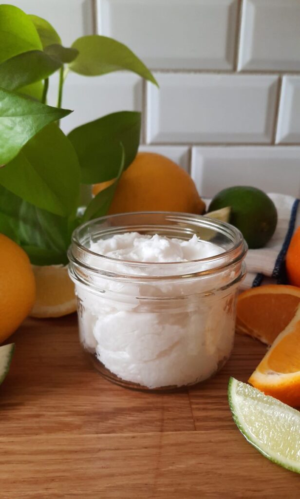 small mason jar full of cream kitchen cleaner scrub surrounded by slices of citrus fruits