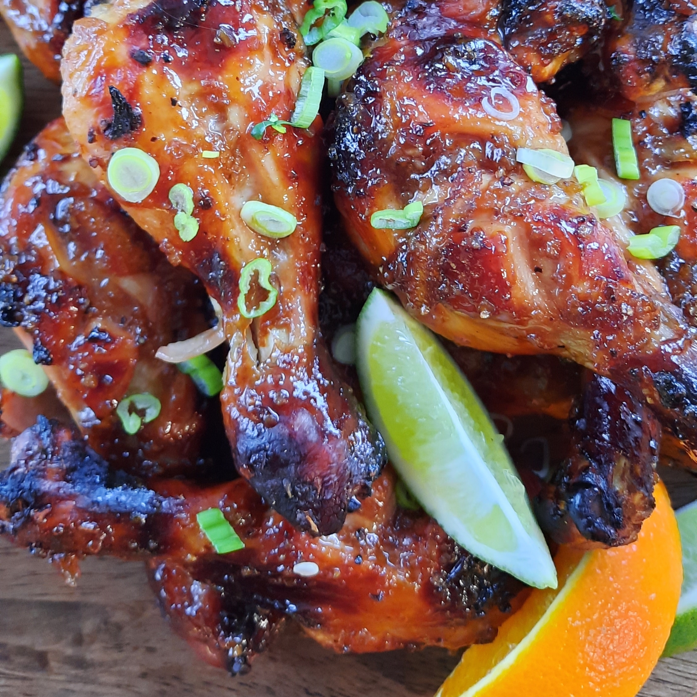 close up of sticky and sweet chicken drumstics with slices of orange and lime